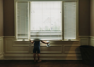 Rear view of boy with toy looking through window