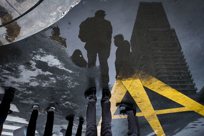 Low section of people standing on road with reflecting in puddle