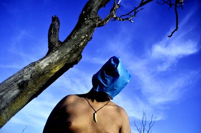 Low angle view of man on tree trunk against blue sky