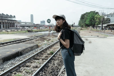 Side view of young woman standing on railroad track against sky