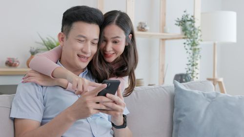 Young woman using mobile phone while sitting on bed at home