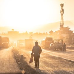 Rear view of man standing on road against sky during sunset