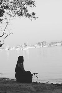 Rear view of woman sitting on sea against sky