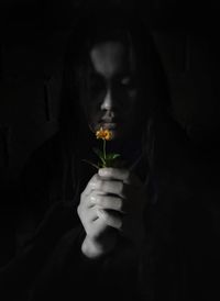 Portrait of woman holding flower in dark room