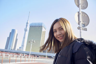 Portrait of smiling young woman in city against sky