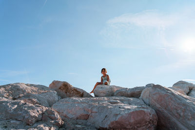 Low angle view of girl standing on rock against sky