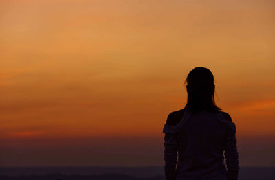 Rear view of silhouette woman standing against orange sky