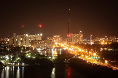 Illuminated city and harbor against sky at night