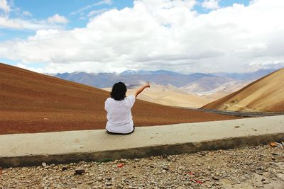 Rear view of woman sitting on landscape against sky