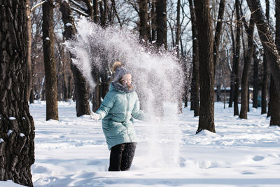 Happy girl in warm clothes throws snow in the winter forest. walk outdoors.