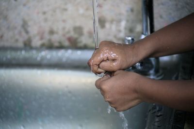 Cropped image of child washing hands at faucet