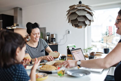 Mother and daughter having food while woman using laptop at dining table