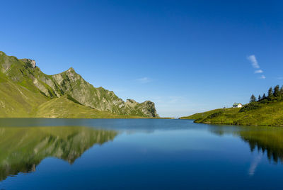 Scenic view of calm lake and mountain against blue sky