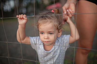 Cute girl looking away while standing with mother by fence