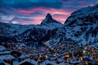 Snow covered houses and mountains against sky during sunset