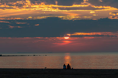 Silhouette woman on sea shore against sky during sunset