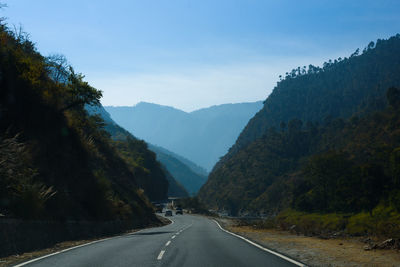 Country road along trees and mountains against sky