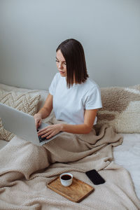 Young woman working on laptop at home in bed