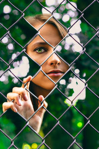 Portrait of young woman seen through chainlink fence