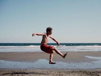 Full length and side view of boy jumping on beach