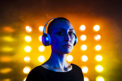 Serious young woman wearing headphones in front of neon lights