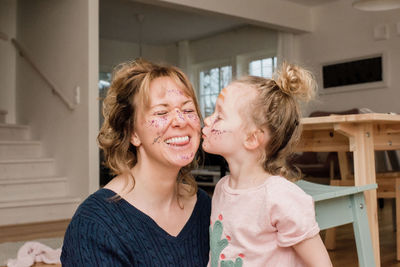 Mother and daughter playing with make up at home laughing together