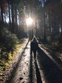 Rear view of man walking with dog on road in forest