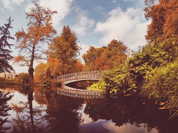 Bridge over river amidst trees against sky during autumn