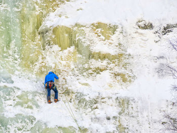 Rear view of man climbing on frozen mountain during winter