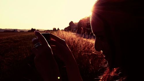 Close-up of woman photographing on field against sky during sunset