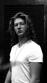 Portrait of young man with long hair standing against wall