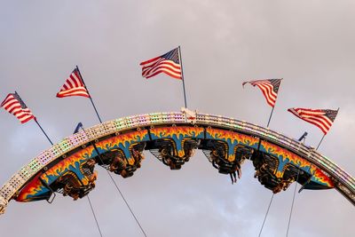Low angle view of flags at amusement park against sky