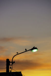 Low angle view of silhouette street light against orange sky