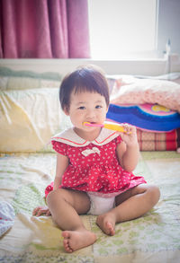 Portrait of cute girl brushing teeth on bed at home