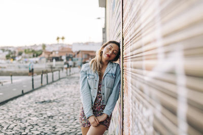 Young woman leaning on wall on footpath