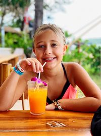 Portrait of smiling girl drinking while sitting on table