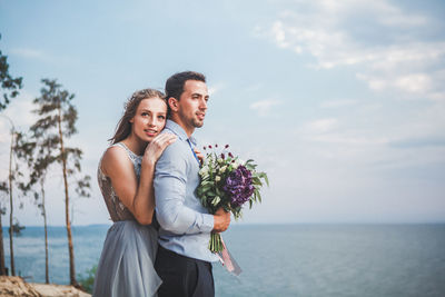 Young couple holding flower against sky