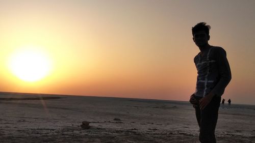 Silhouette man standing on beach at sunset