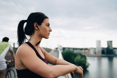 Side view of female athlete looking away while standing on footbridge in city