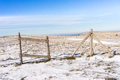 Fence on snow covered field against sky