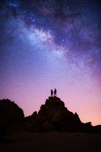 Silhouette couple standing on rock formation against sky at night