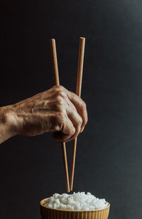 Close-up of hand holding chopsticks against black background