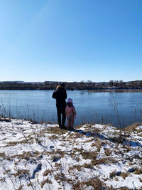 Rear view of man standing in lake against sky during winter