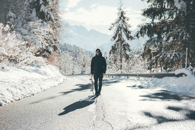 Full length of man holding skateboard while walking on road