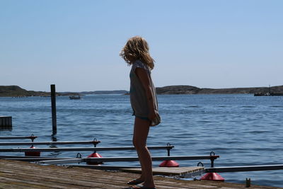 Rear view of young woman standing by sea against clear sky