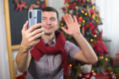 Midsection of man using mobile phone on christmas tree