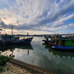 Boats moored in harbor at sunset