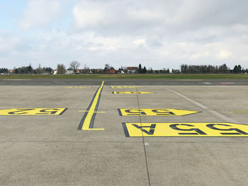 Yellow arrow symbol on airport runway against sky