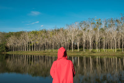 Rear view of woman in hood clothing by lake against sky