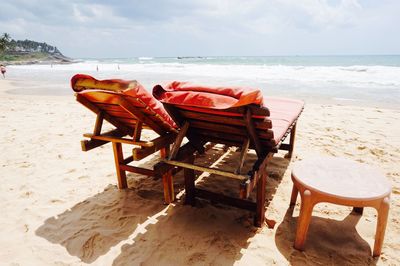 Deck chairs by table at beach against sky